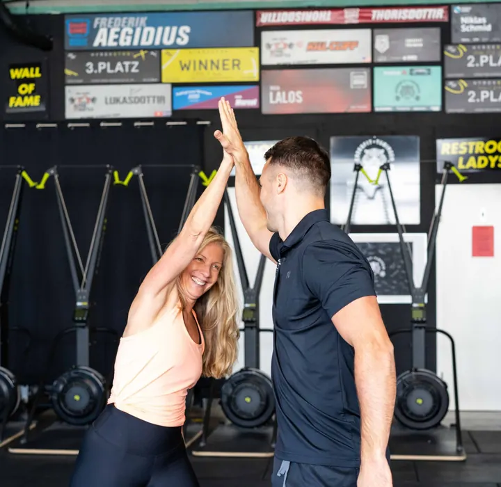 Kundin und Coach geben sich ein High-Five vor der Wall of Fame im Studio